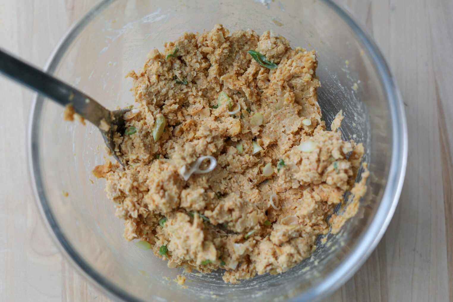Smashed Chickpea Tacos 4 A Glass Bowl Filled With A Chunky, Beige Mixture Of Smashed Chickpea Tacos Containing Herbs And Chopped Vegetables, With A Metal Spoon Sticking Out, Sits On A Light Wooden Surface.