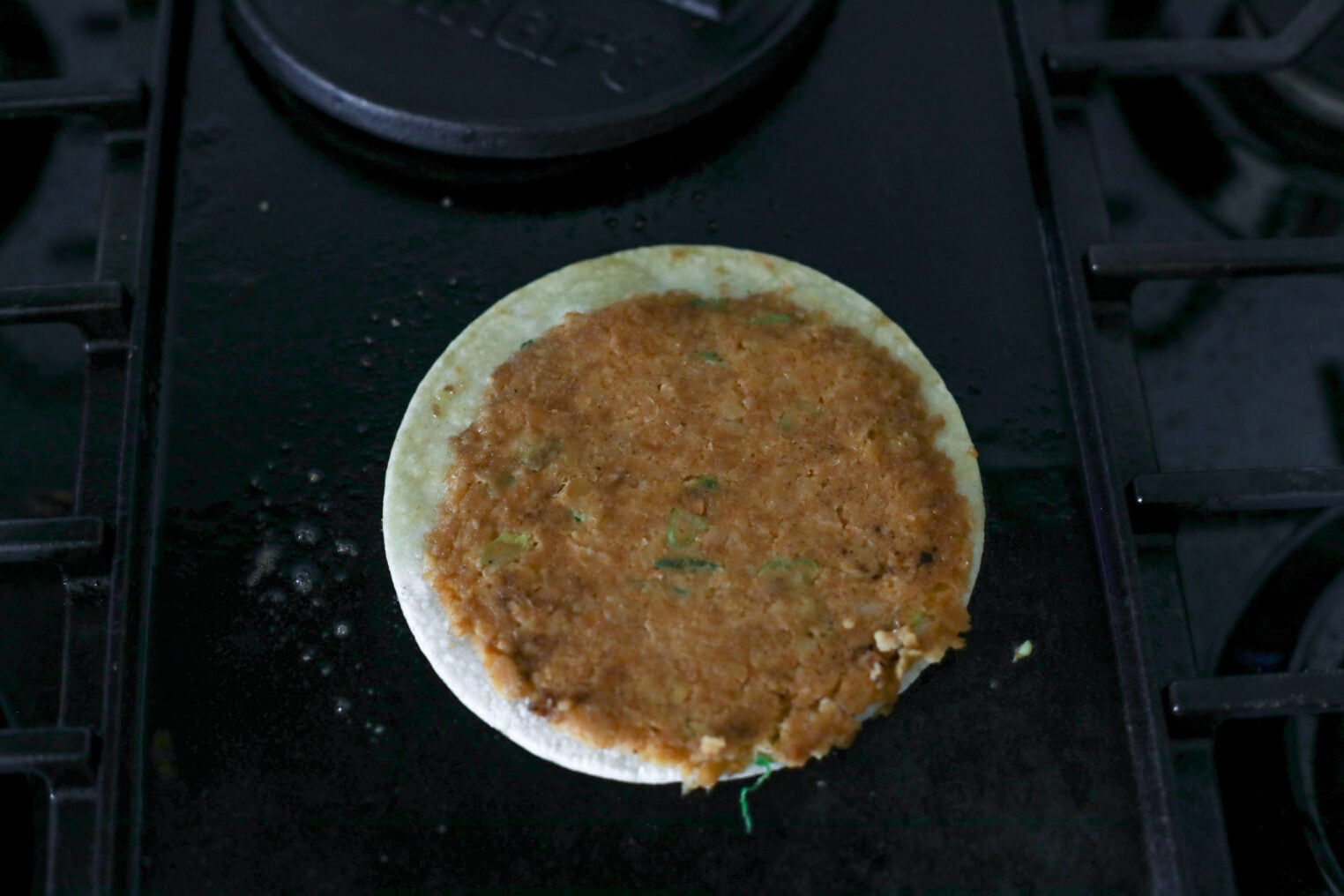 Smashed Chickpea Tacos 8 A Round Veggie Burger Patty Is Heating On A White Corn Tortilla On A Black Stovetop Griddle, Creating The Perfect Base For Delicious Smashed Chickpea Tacos.