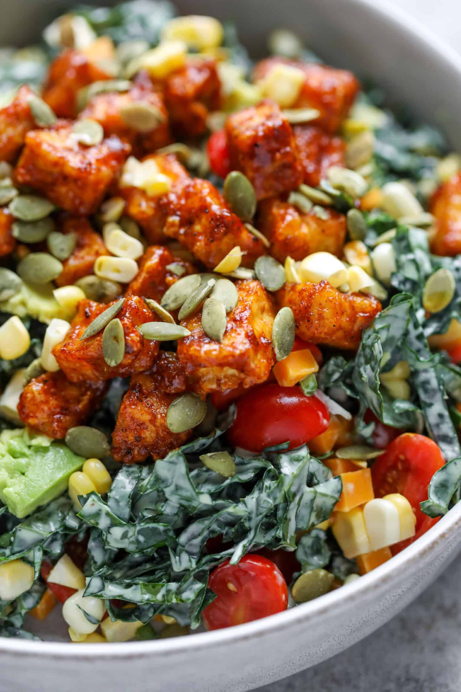 Spicy Kale Salad with Avocado Ranch 8 A Close-Up Of A Spicy Kale Salad Bowl Featuring Chopped Kale, Cherry Tomatoes, Corn, Roasted Tofu Cubes, Pumpkin Seeds, And A Creamy Dressing. The Vibrant Ingredients Create A Colorful And Appetizing Dish.