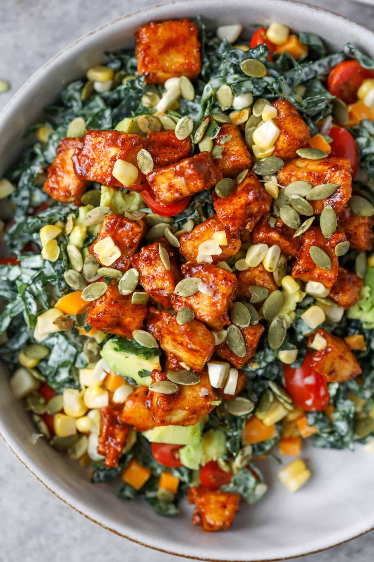Spicy Kale Salad with Avocado Ranch 1 A Bowl Filled With Spicy Kale Salad Topped With Roasted Tofu Cubes, Cherry Tomatoes, Corn, Avocado, Diced Bell Peppers, And Sprinkled With Pumpkin Seeds.
