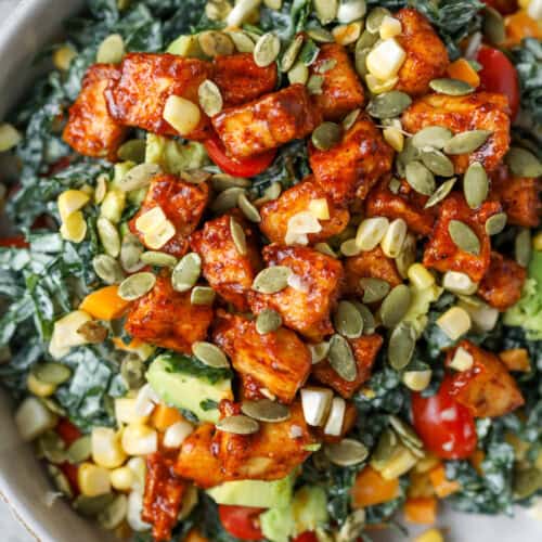 Spicy Kale Salad with Avocado Ranch 10 A Bowl Filled With Spicy Kale Salad Topped With Roasted Tofu Cubes, Cherry Tomatoes, Corn, Avocado, Diced Bell Peppers, And Sprinkled With Pumpkin Seeds.