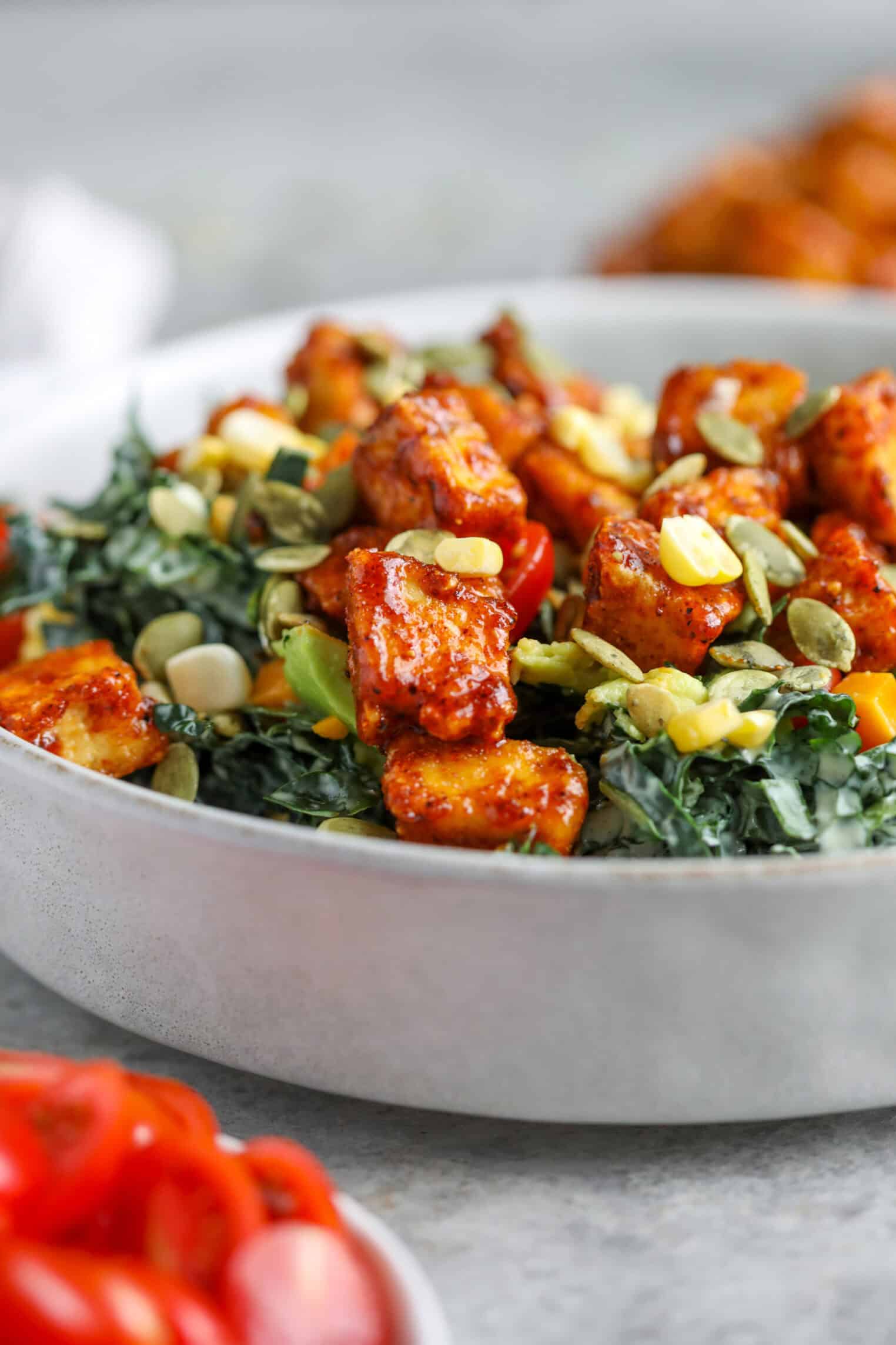 Spicy Kale Salad with Avocado Ranch 3 A Bowl Of Spicy Kale Salad Topped With Crispy, Seasoned Tofu Cubes, Corn, Pumpkin Seeds, And Cherry Tomatoes, With Chopped Greens As The Base.