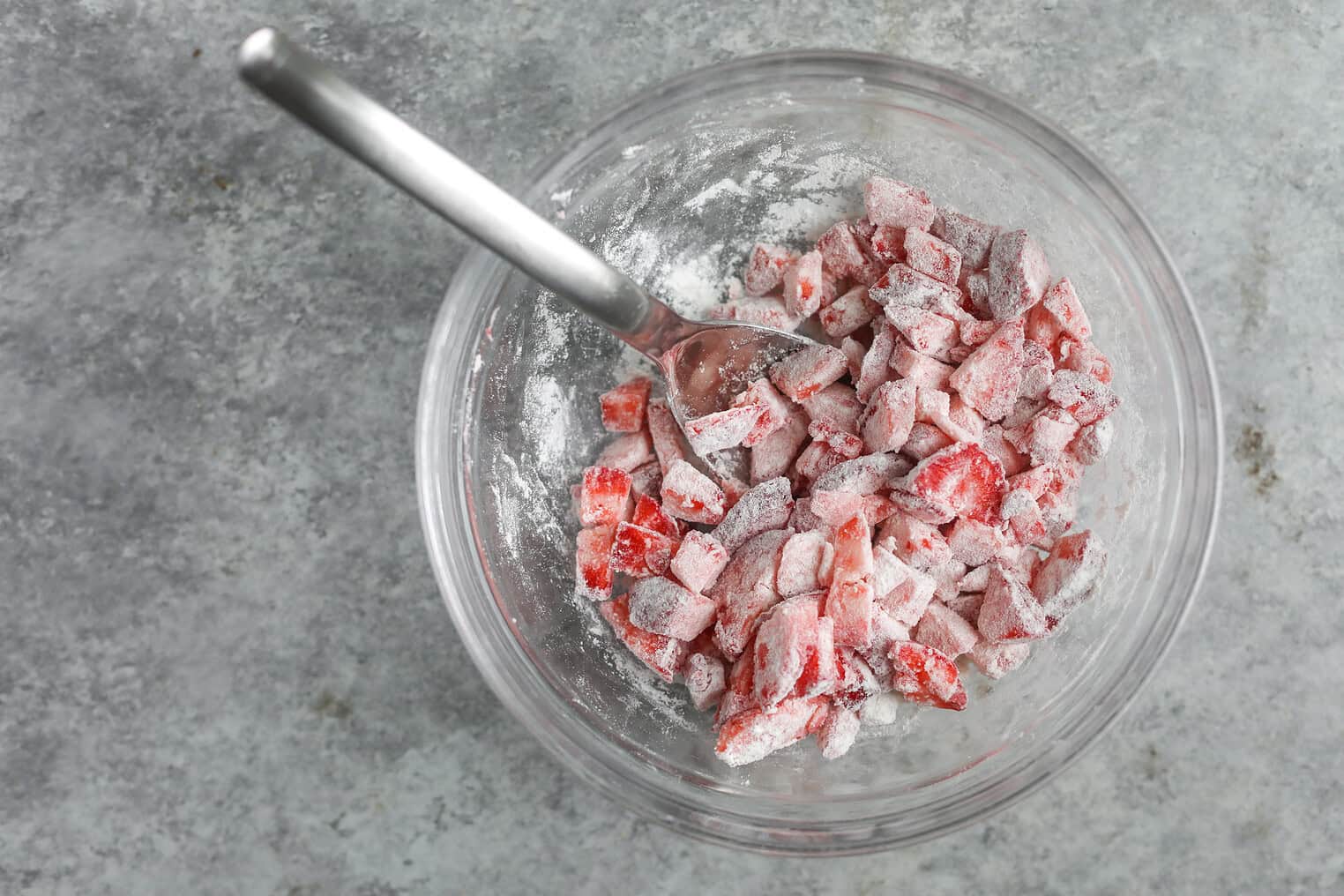 Vegan Strawberry Lemonade Scones 6 A Glass Bowl Filled With Chopped Strawberries Coated In Flour, Perfect For Lemonade Scones, Sits With A Metal Spoon Inside On A Gray Textured Surface.