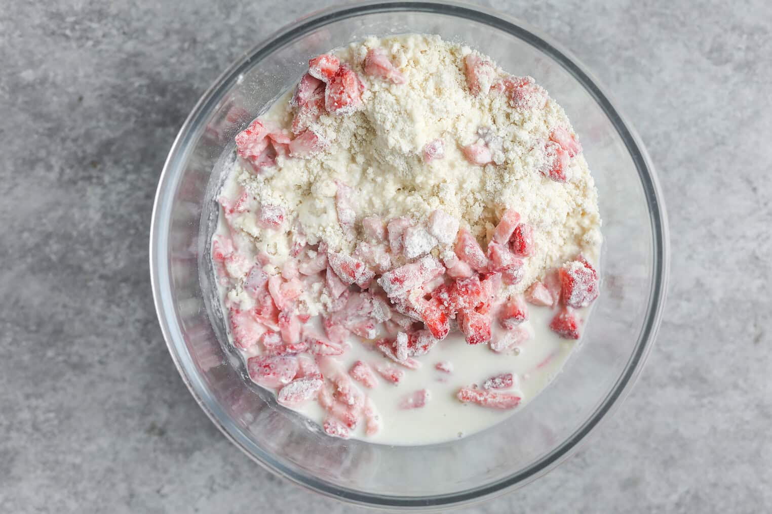 Vegan Strawberry Lemonade Scones 9 A Glass Bowl Containing Chopped Strawberries, Milk, And Flour Mixture—Perfect For Preparing Vegan Scones—On A Gray Surface, Viewed From Above.