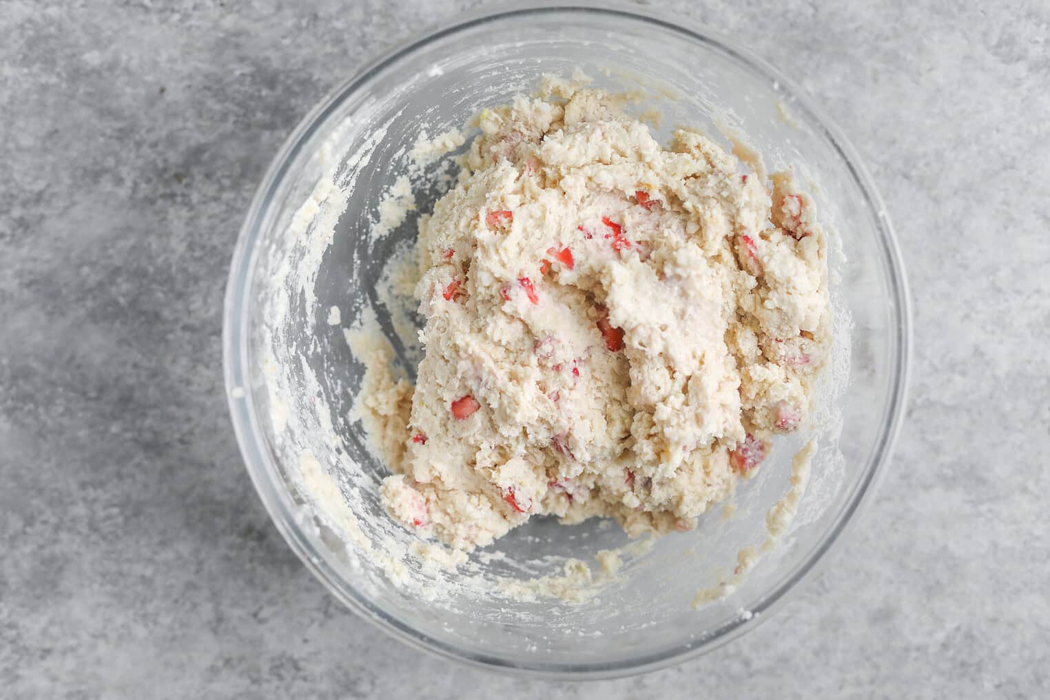 Vegan Strawberry Lemonade Scones 10 A Glass Bowl Filled With Unbaked Dough For Vegan Scones, Featuring Visible Small Red Pieces, Sits On A Gray Textured Surface.