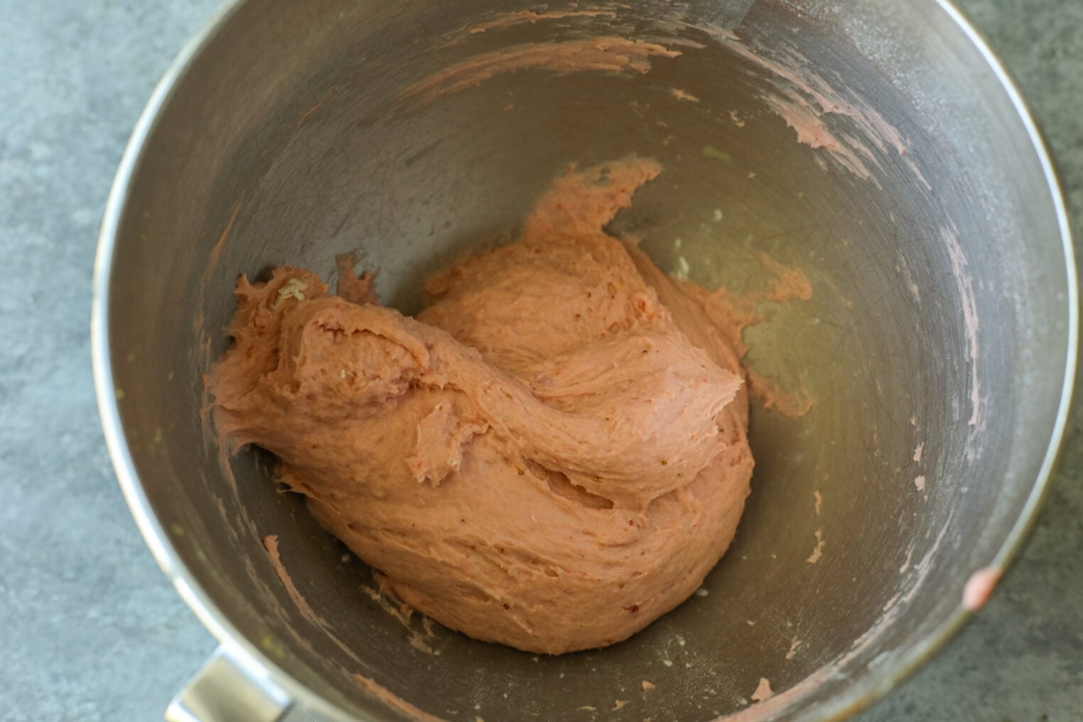 A Metal Mixing Bowl Containing A Thick, Pinkish Strawberry Rolls Dough, Partially Mixed And Sticking To The Sides, Sits On A Gray Countertop.
