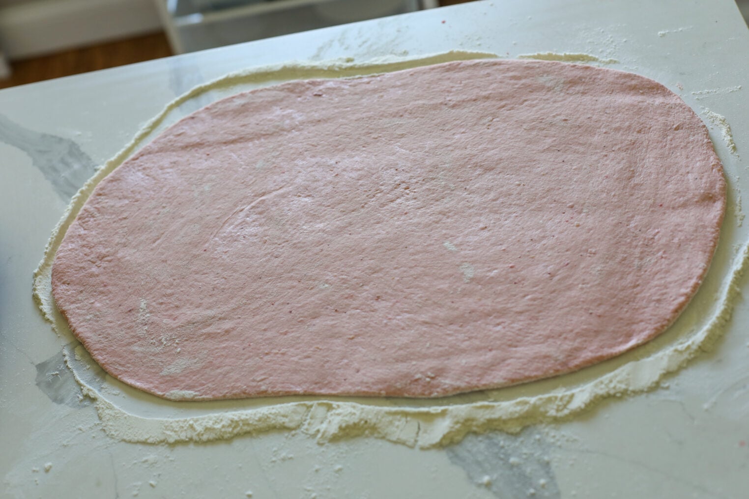 A Large Oval Sheet Of Pink Dough, Perfect For Strawberry Rolls, Is Rolled Out On A Floured White Surface, Ready For Baking Or Cooking.