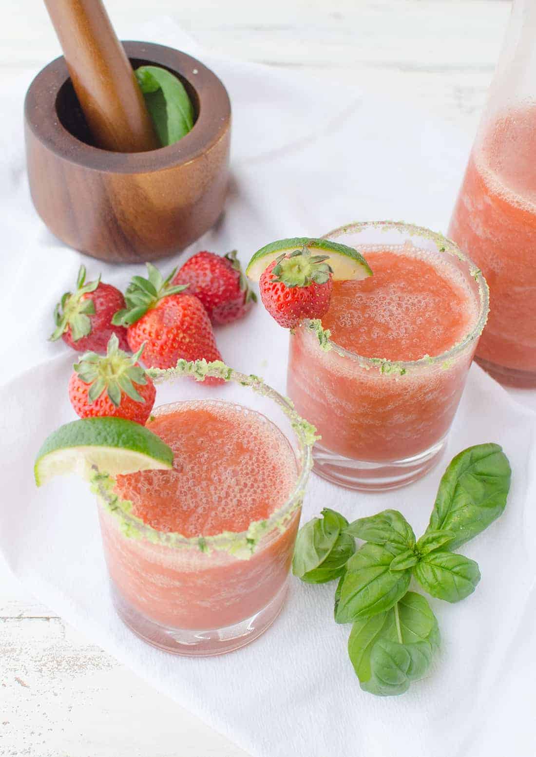 Top Down Image Showing The Strawberry Margaritas With The Basil-Salt Rim And Fresh Strawberries To Garnish