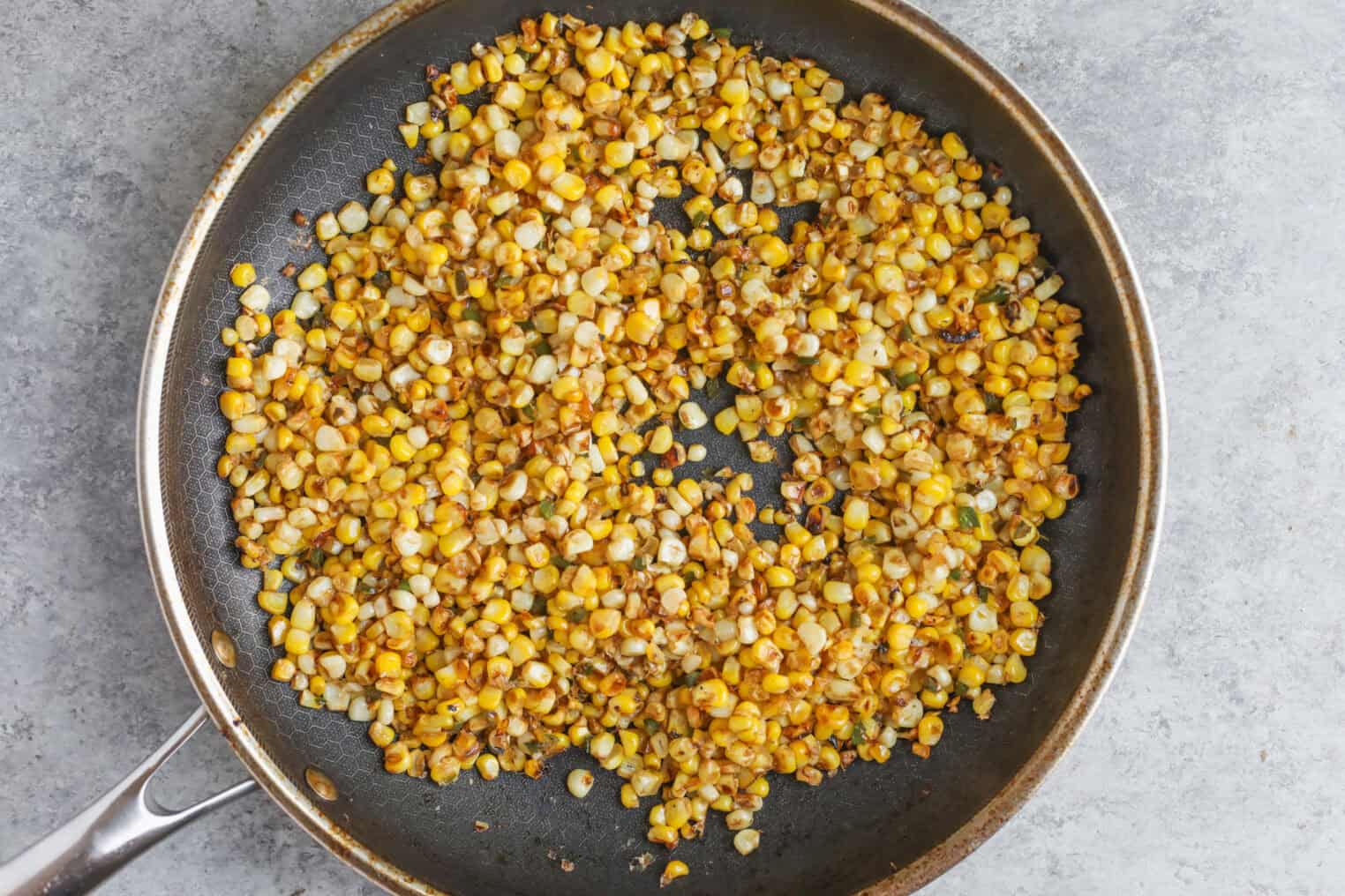 Easy Street Corn Tostadas 4 A Frying Pan Filled With Sautéed Corn Kernels, Lightly Browned And Golden, Sits On A Gray Countertop. The Corn Appears Cooked And Seasoned, Perfect As A Topping For Street Corn Tostadas With Its Caramelized Flavor.