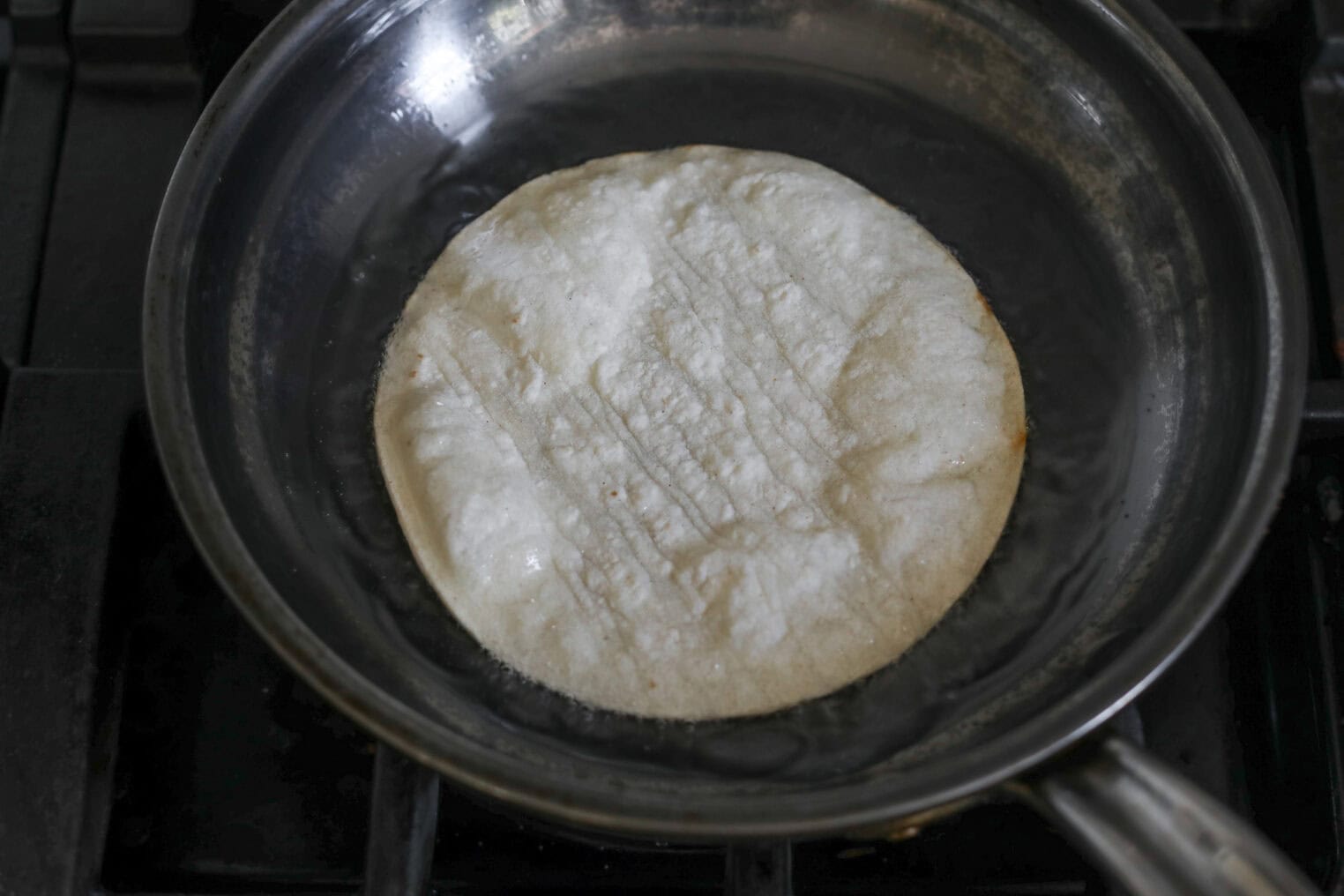 Easy Street Corn Tostadas 7 A Corn Tortilla Is Being Fried In Oil In A Skillet On A Stovetop, With Bubbles Forming On The Surface As It Cooks—Perfect For Making Crispy Street Corn Tostadas.