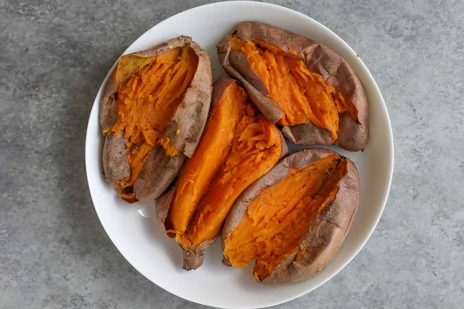 Vegan Stuffed Sweet Potatoes 8 A White Plate Holds Several Vegan Stuffed Sweet Potatoes Cut Open, Revealing Their Bright Orange, Fluffy Interiors Against A Gray Surface Background.