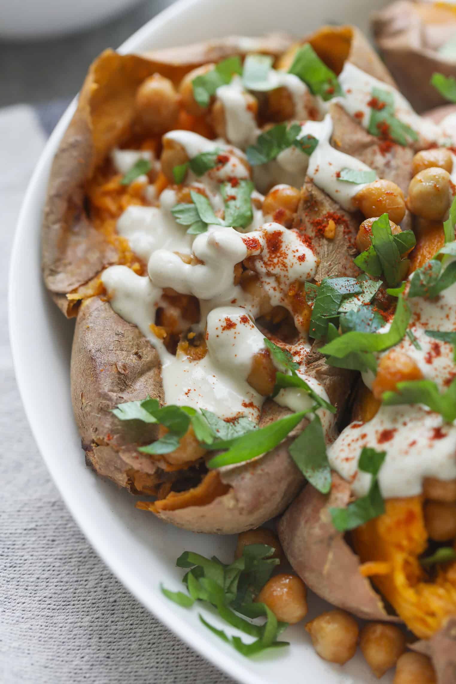 Vegan Stuffed Sweet Potatoes 4 Close-Up Of Vegan Stuffed Sweet Potatoes Topped With Roasted Chickpeas, Creamy White Sauce, Chopped Fresh Herbs, And A Sprinkle Of Paprika, Served In A White Bowl.