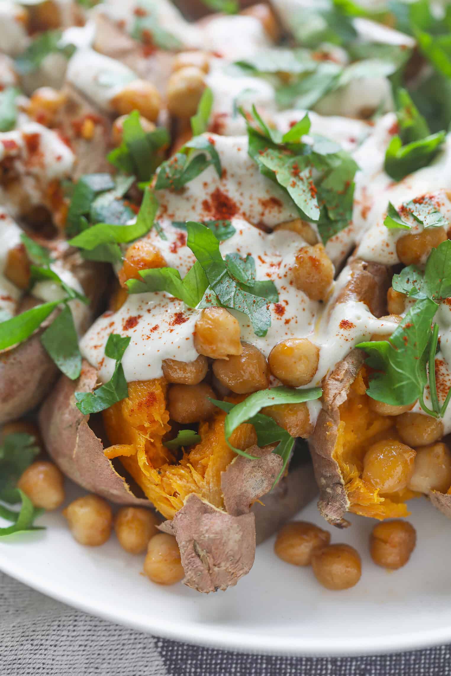 Vegan Stuffed Sweet Potatoes 1 Vegan Stuffed Sweet Potatoes Topped With Roasted Chickpeas, Creamy White Sauce, Fresh Chopped Parsley, And A Sprinkle Of Paprika, Served On A White Plate.