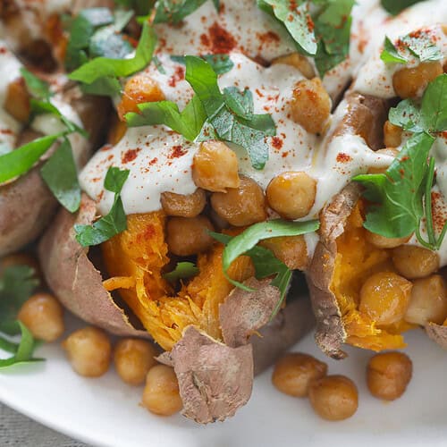 Vegan Stuffed Sweet Potatoes 12 Vegan Stuffed Sweet Potatoes Topped With Roasted Chickpeas, Creamy White Sauce, Fresh Chopped Parsley, And A Sprinkle Of Paprika, Served On A White Plate.