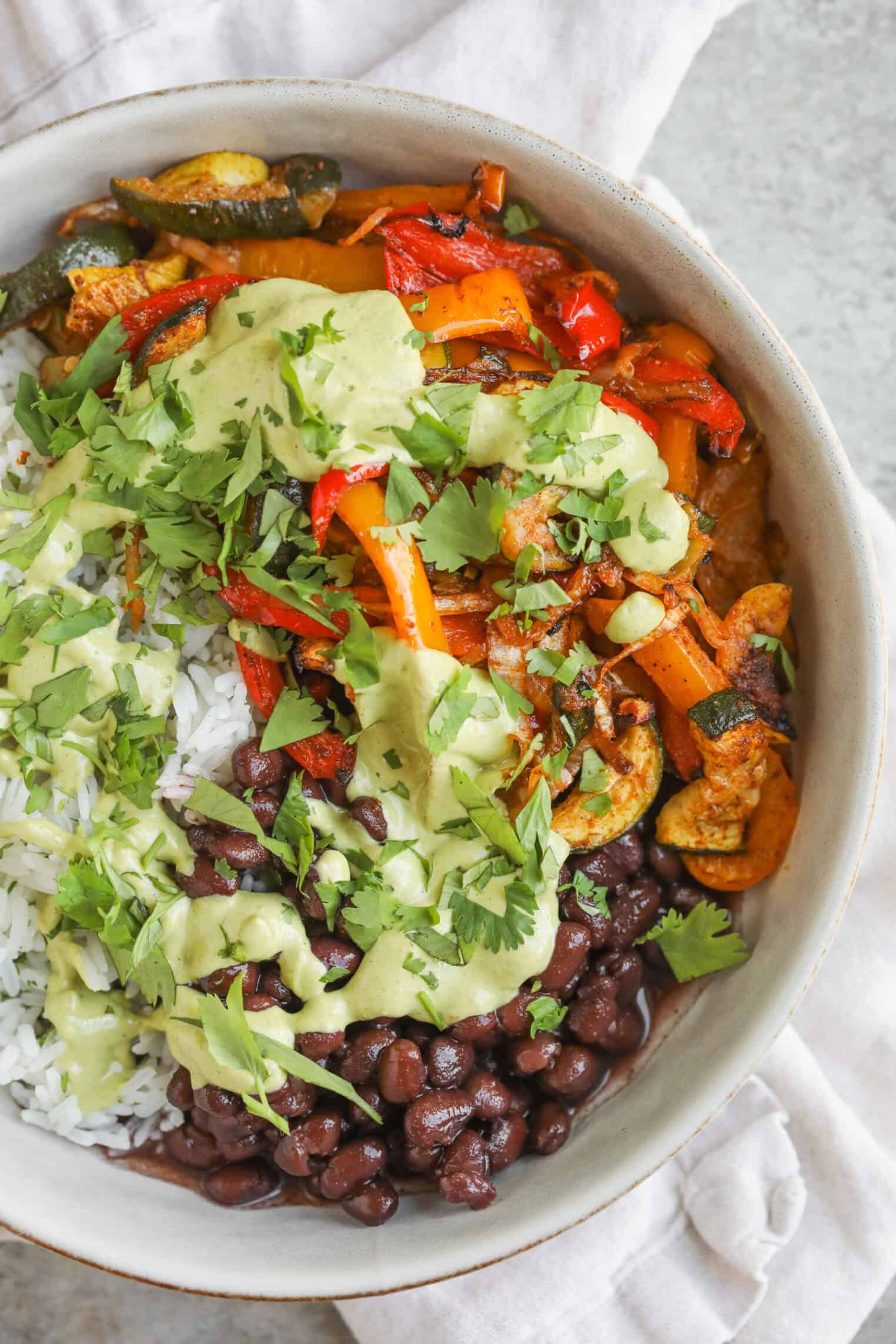 A Bowl Filled With White Rice, Black Beans, Sautéed Red And Yellow Bell Peppers, Zucchini, And Avocado Cilantro Dressing, Garnished With Fresh Cilantro—Perfect For Enjoying Vibrant Summer Fajita Bowls.