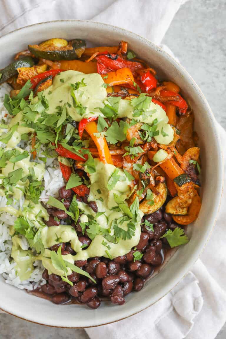 A Bowl Filled With White Rice, Black Beans, Sautéed Red And Yellow Bell Peppers, Zucchini, And Avocado Cilantro Dressing, Garnished With Fresh Cilantro—Perfect For Enjoying Vibrant Summer Fajita Bowls.