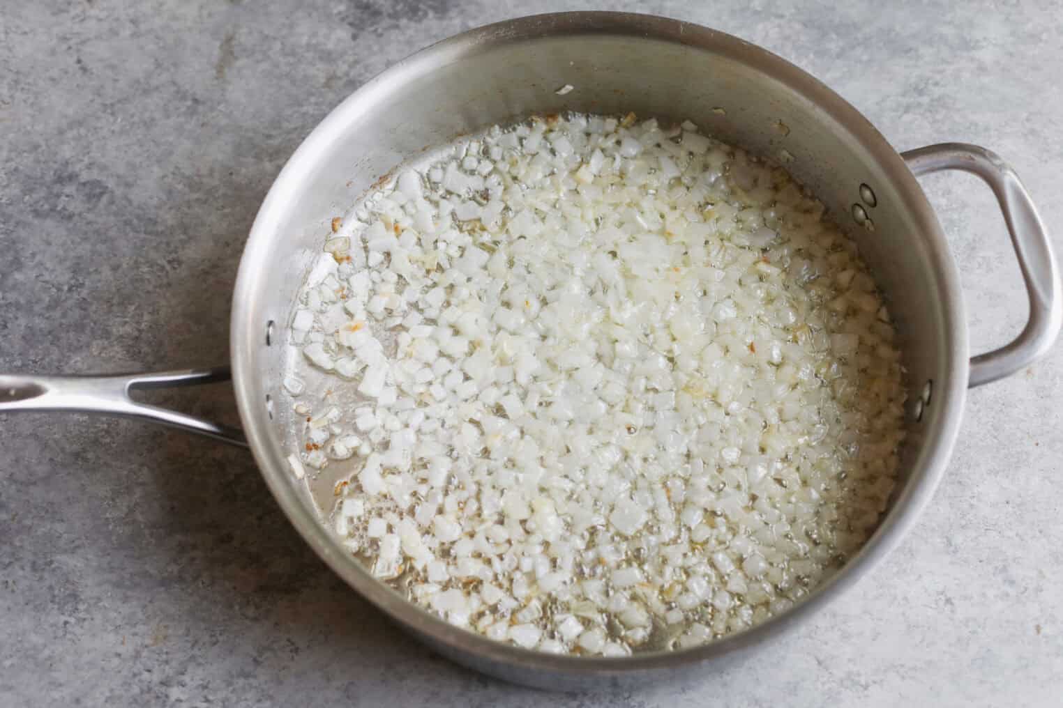 Chopped Onions Being Sautéed In Oil In A Stainless Steel Pan On A Gray Countertop, Ready To Be Added To Summer Gnocchi With Fresh Corn And Zucchini Sauce.