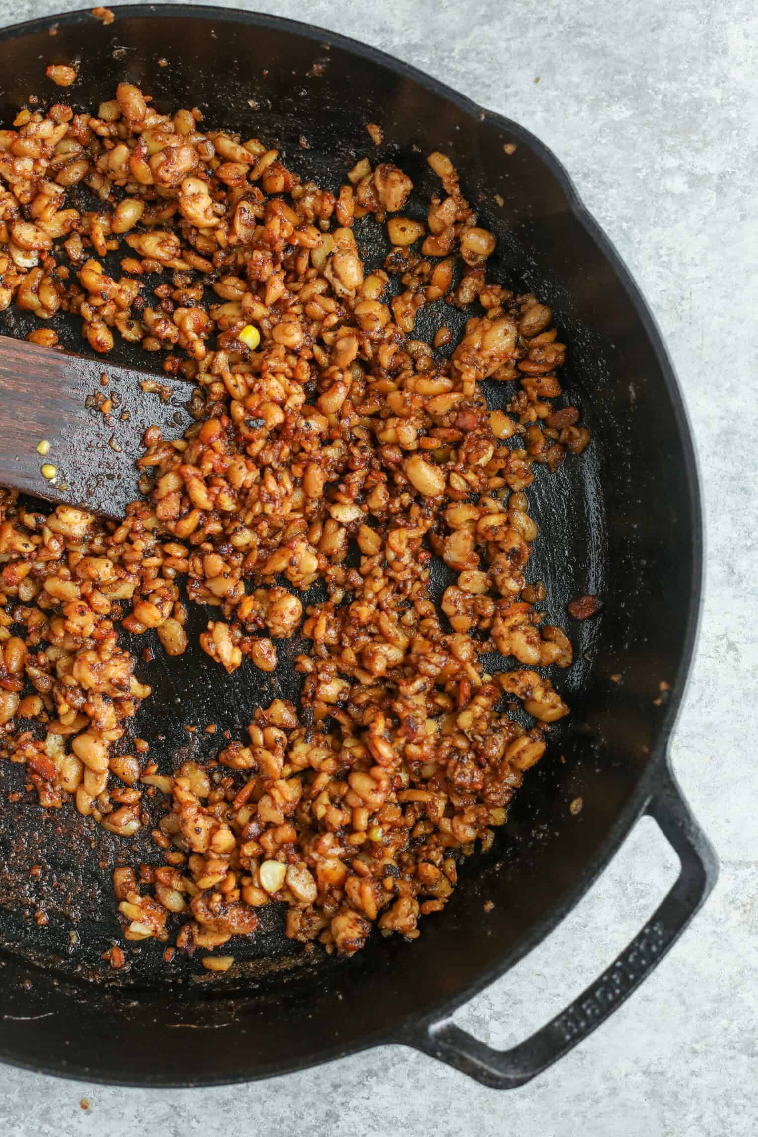 A Cast-Iron Skillet Filled With Sautéed, Diced White Beans Mixed With Spices And Seasonings, Perfect As A Hearty Topping For A Summer Wedge Salad. A Wooden Spatula Rests In The Pan, Set Against A Light Gray Surface.