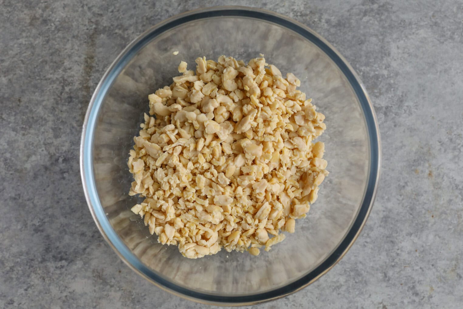 A Clear Glass Bowl Filled With Crumbled Tempeh Sits On A Grey, Textured Countertop—Perfect For Adding Protein To Your Summer Wedge Salad.