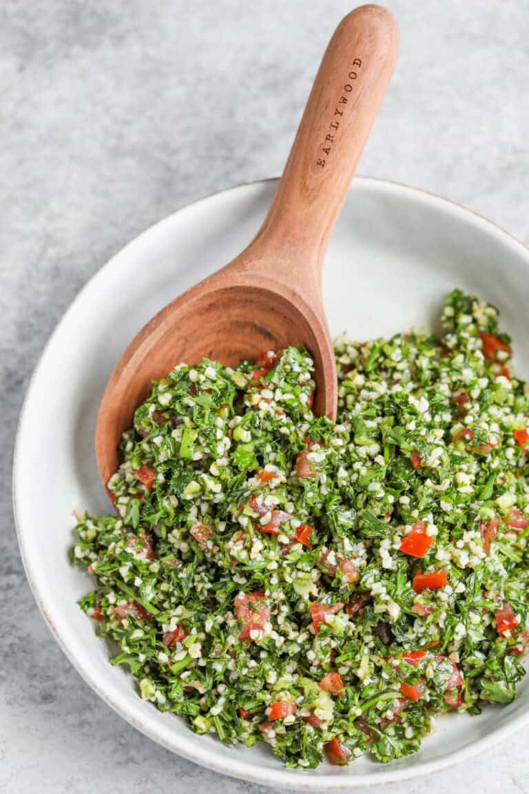 A Vibrant Mediterranean Salad, This Bowl Of Fresh Tabbouleh Features Chopped Parsley, Tomatoes, Bulgur, And Herbs, Served With A Wooden Spoon On A Light Gray Background.