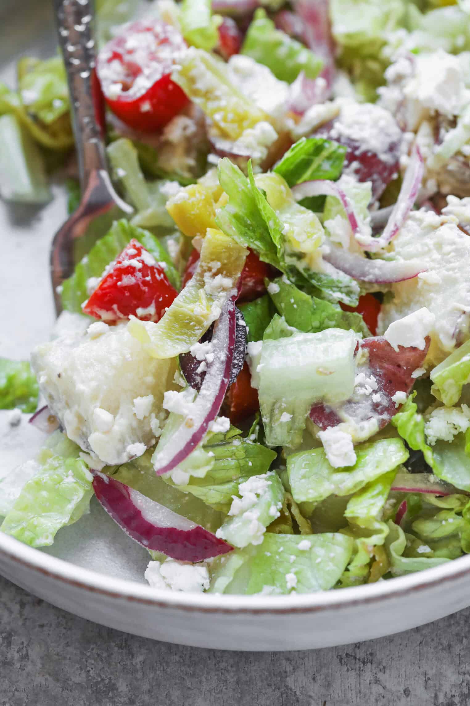 A Close-Up Of A Fresh Tarpon Springs Greek Salad With Lettuce, Tomatoes, Red Onions, Cucumbers, Banana Peppers, Crumbled Feta Cheese, And Classic Potato Salad On A Plate With A Fork.