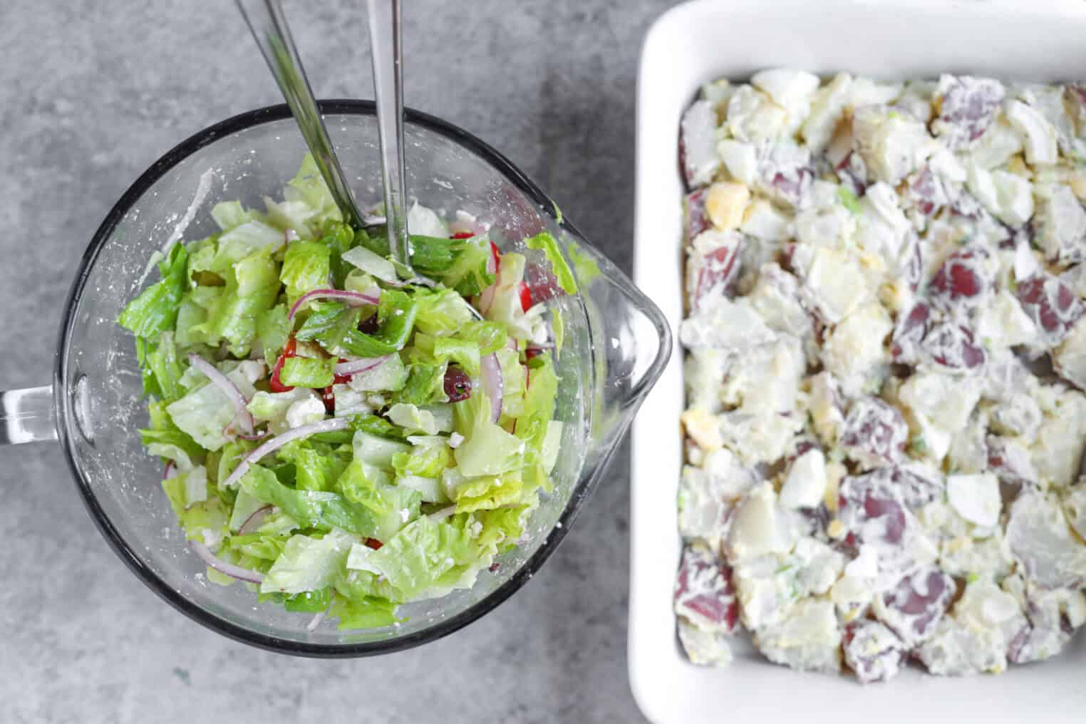 A Glass Bowl Of Green Salad With Lettuce, Radishes, And Onions Sits Beside A White Dish Filled With Creamy Potato Salad—Reminiscent Of A Tarpon Springs Greek Salad With Potato Salad—On A Gray Surface.