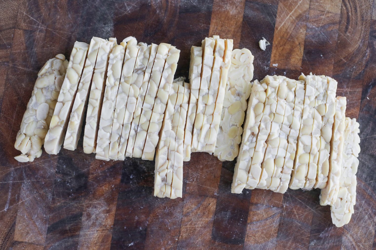 Teriyaki Tempeh Stir Fry 3 Sliced Tempeh Arranged On A Dark Wooden Cutting Board, Highlighting The Textured Appearance Of This Soybean-Based Product Perfect For A Flavorful Tempeh Stir Fry.