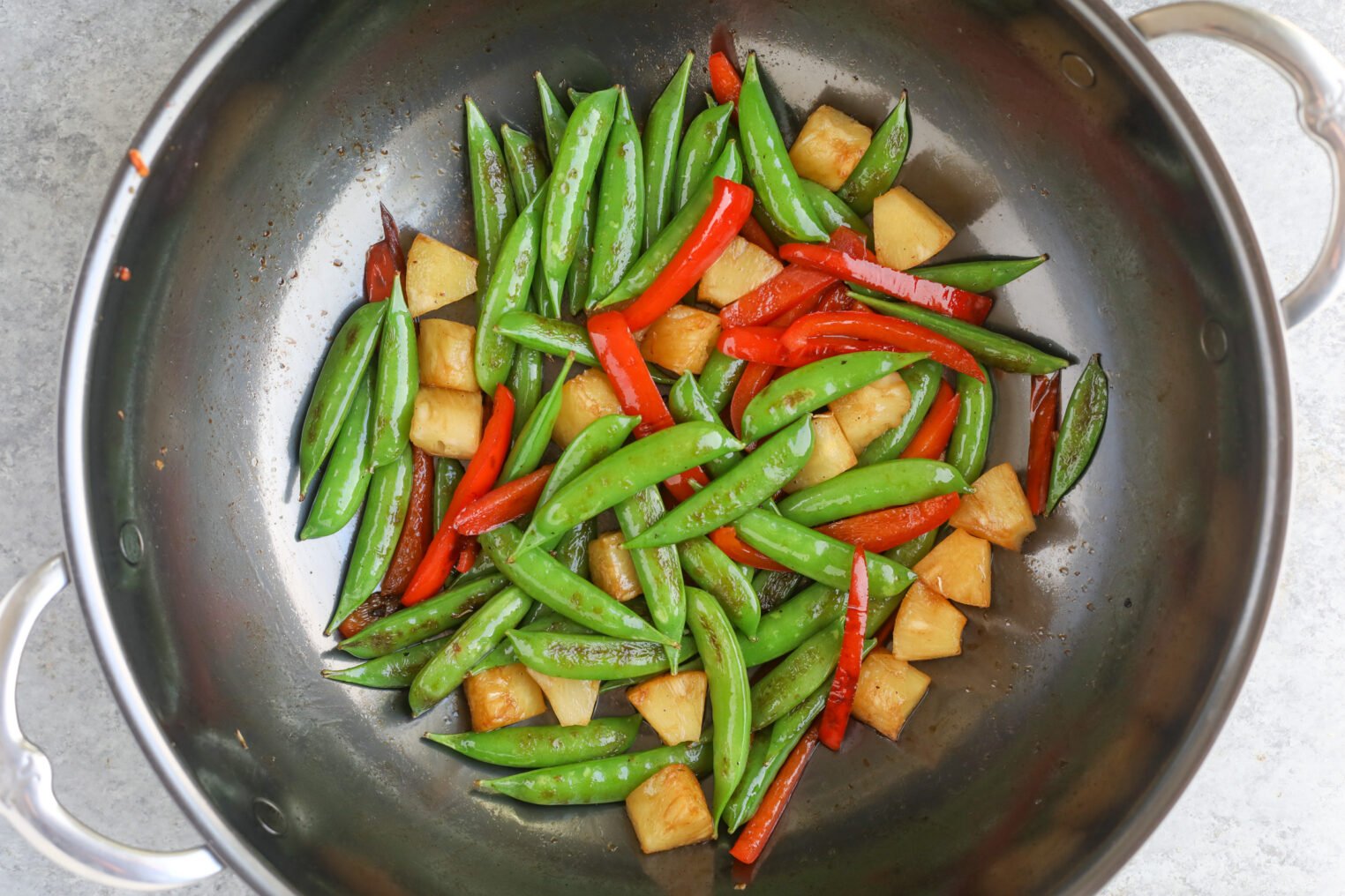 Teriyaki Tempeh Stir Fry 5 A Wok Filled With Cooked Snap Peas, Red Bell Pepper Strips, And Pineapple Chunks Sits On A Light Gray Surface, Showcasing This Vibrant, Glossy Tempeh Stir Fry. The Vegetables And Fruit Add A Burst Of Color And Freshness.