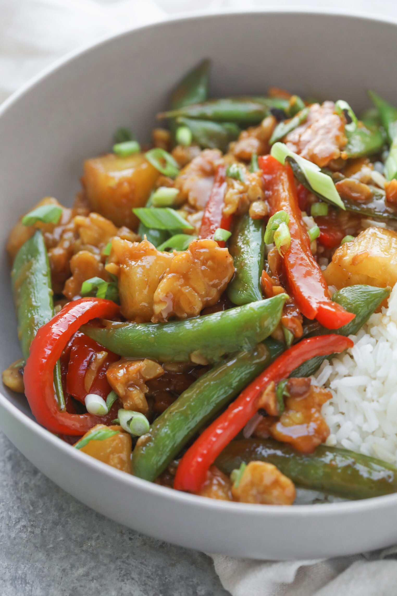 Teriyaki Tempeh Stir Fry 1 A Bowl Of Tempeh Stir Fry With White Rice, Featuring Snap Peas, Red Bell Peppers, Pineapple Chunks, Green Onions, And Pieces Of Chicken In A Glossy Sauce.