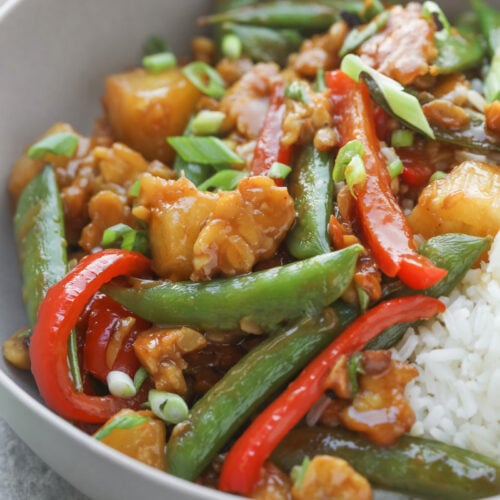 Teriyaki Tempeh Stir Fry 10 A Bowl Of Tempeh Stir Fry With White Rice, Featuring Snap Peas, Red Bell Peppers, Pineapple Chunks, Green Onions, And Pieces Of Chicken In A Glossy Sauce.