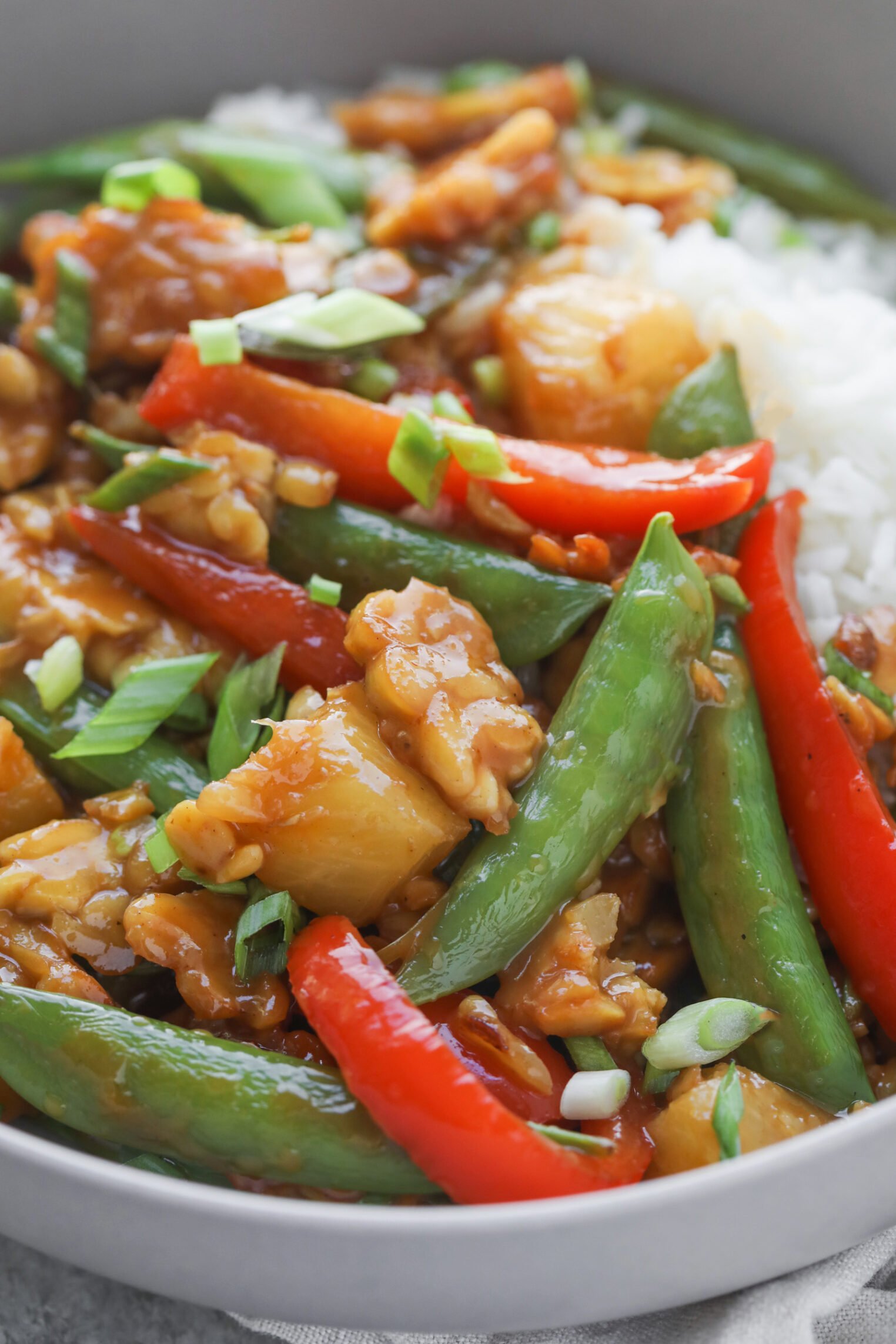 Teriyaki Tempeh Stir Fry 7 A Close-Up Of A Colorful Tempeh Stir Fry With Snap Peas, Red Bell Peppers, Pineapple Chunks, Green Onions, And Pieces Of Chicken In A Savory Sauce, Served Alongside White Rice.