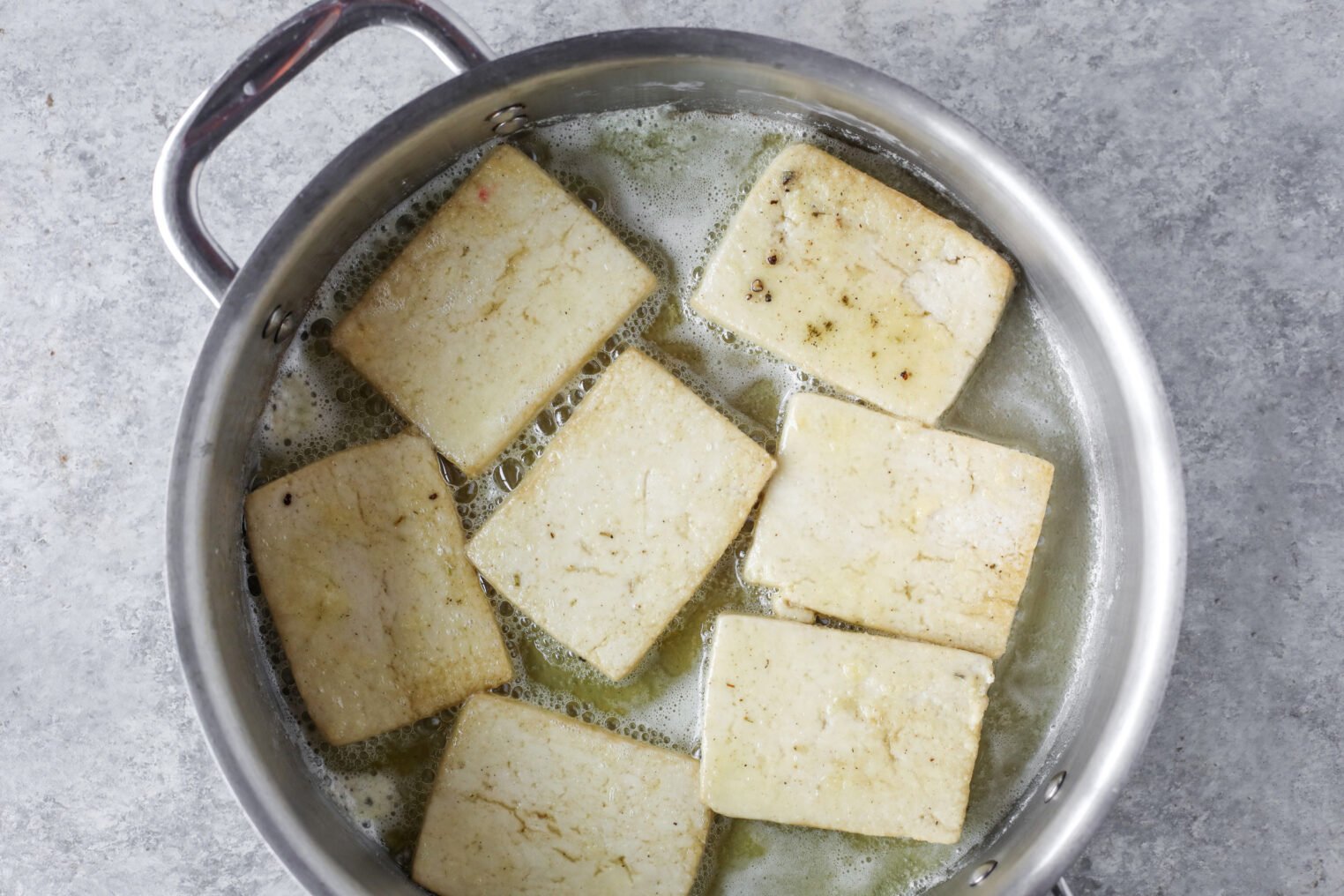 Sliced Tofu Pieces, Perfect For Tofu Piccata, Are Being Boiled In Water Inside A Stainless Steel Pot, Viewed From Above On A Gray Countertop.
