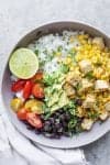 vegan rice bowl with beans, cilantro lime tofu, corn and a lime wedge