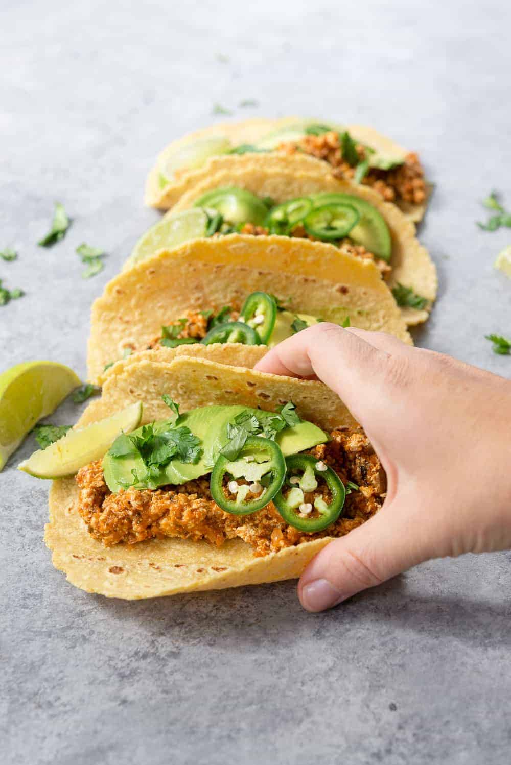 vegan tofu tinga tacos on grey surface with hand