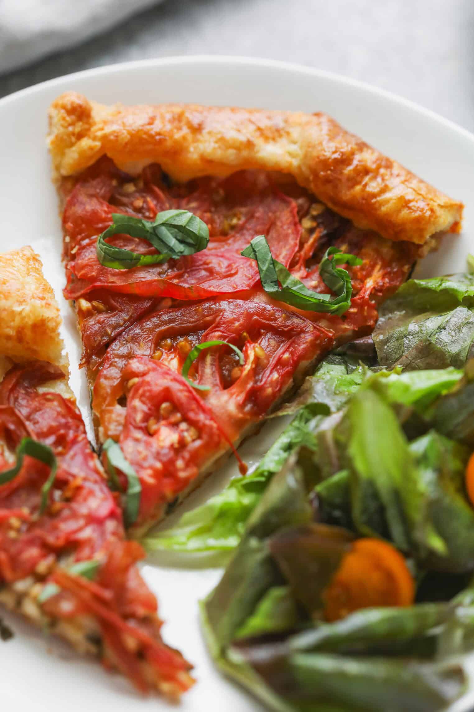 Tomato Galette 12 A White Plate With A Slice Of Tomato Galette Topped With Fresh Basil, Next To A Green Salad With Leafy Greens And Sliced Cherry Tomatoes.