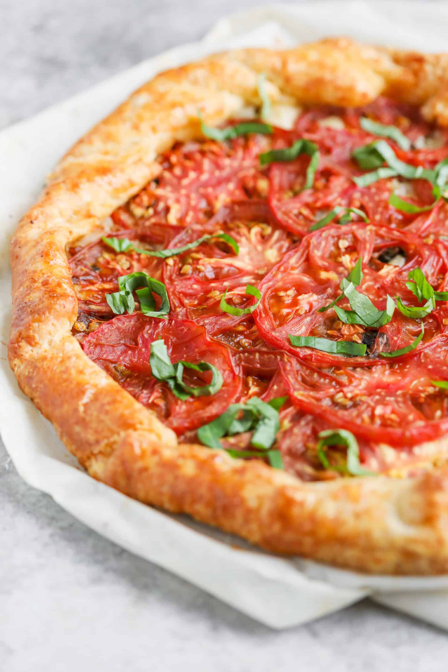 Tomato Galette 11 A Rustic Tomato Galette With A Golden, Flaky Crust, Topped With Fresh Tomato Slices And Chopped Basil, Sits On Parchment Paper—Perfect For Showcasing The Simple Elegance Of A Homemade Tomato Galette.