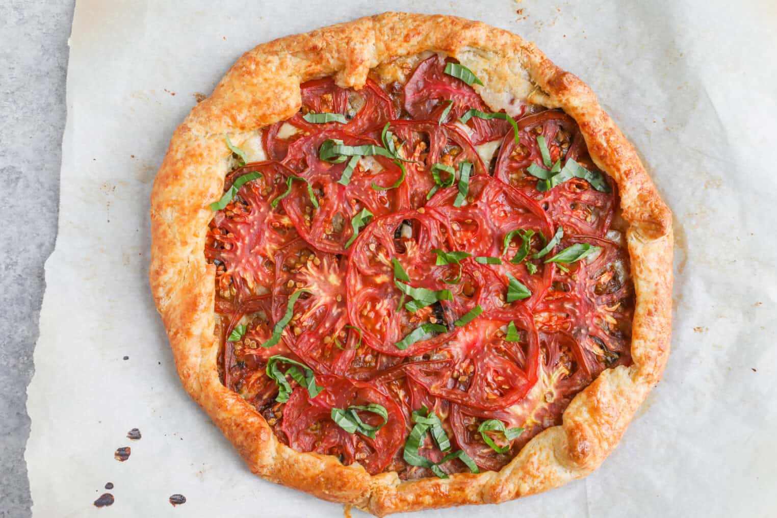 Tomato Galette 10 A Rustic Tomato Galette Sits On Parchment Paper, Its Golden-Brown, Flaky Crust Cradling Juicy Sliced Tomatoes And Fresh Basil Strips—An Inviting Showcase Of This Classic Tomato Galette.