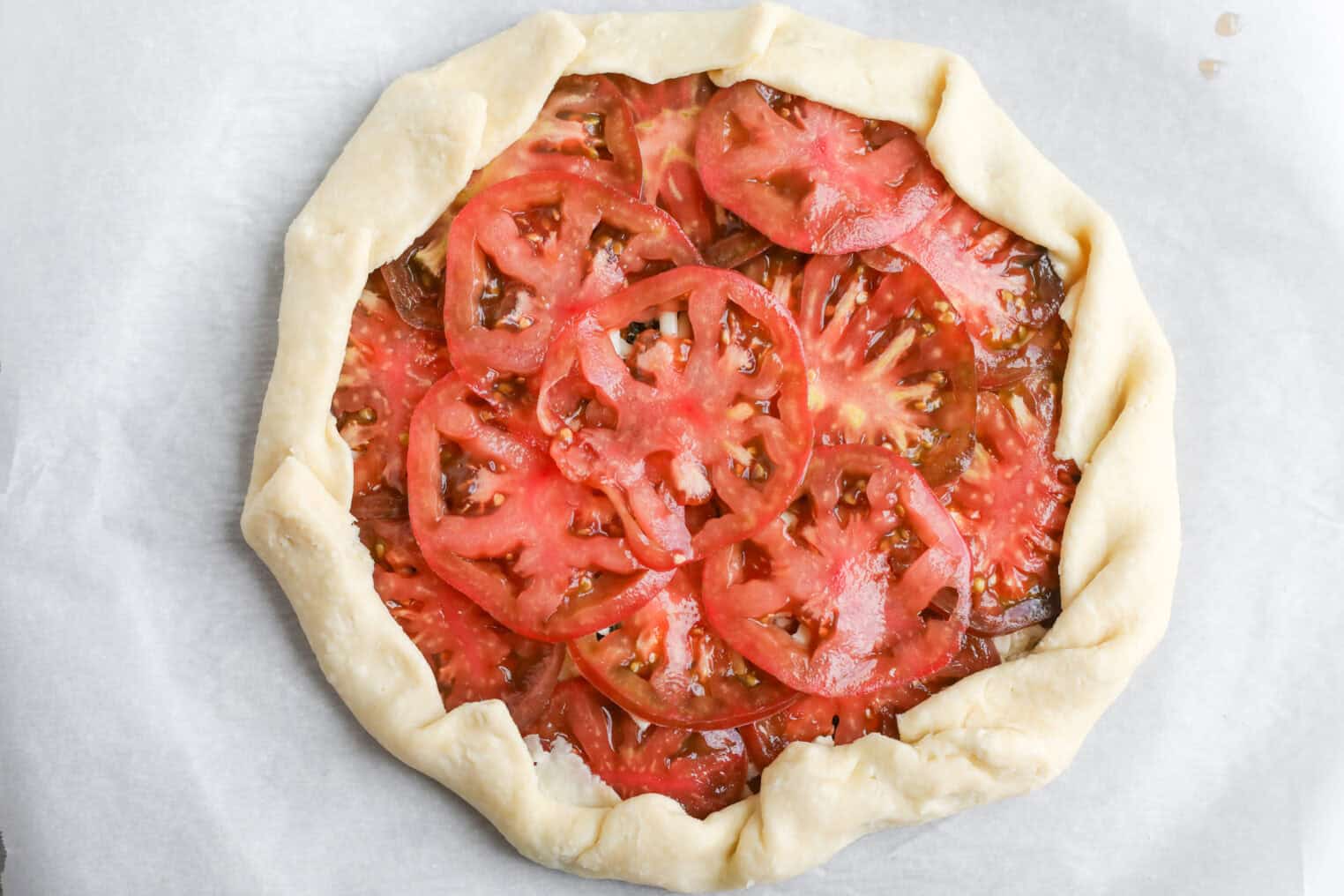 Tomato Galette 9 A Rustic Tomato Galette With Sliced Tomatoes Arranged On A Pastry Crust, Edges Folded Over For A Classic Tomato Galette Look, Resting On White Parchment Paper.