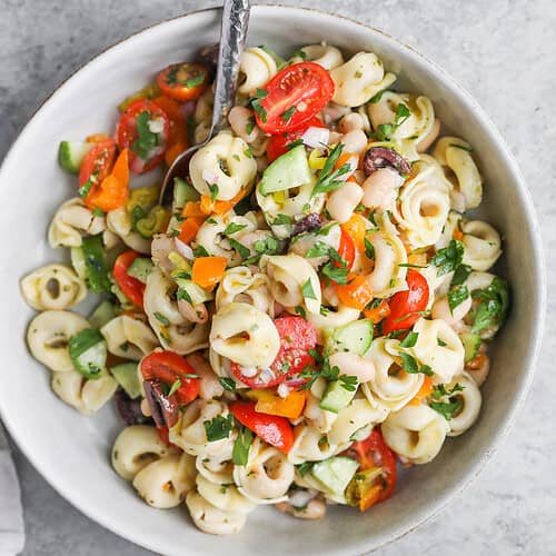Tortellini Pasta Salad 11 A Bowl Of Tortellini Pasta Salad With Cherry Tomatoes, Cucumber, Bell Pepper, Olives, And Parsley Is Served With A Fork. Fresh Parsley And A Bowl Of Pepperoncini Accompany This Vibrant Tortellini Pasta Salad On The Side.
