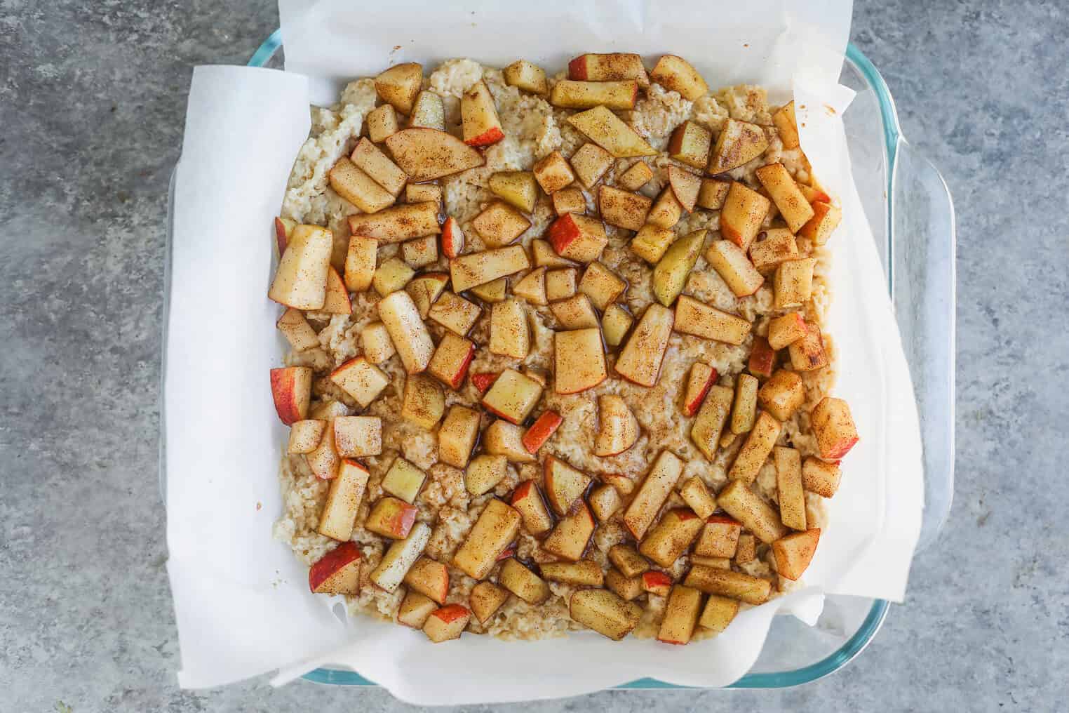 Vegan Apple Cake 8 A Baking Dish Lined With Parchment Paper Holds An Unbaked Oat Crust, Topped With Chopped Apples And Cinnamon Spice—Just Like A Homemade Cinnamon Spice Apple Cake—Ready To Be Baked.
