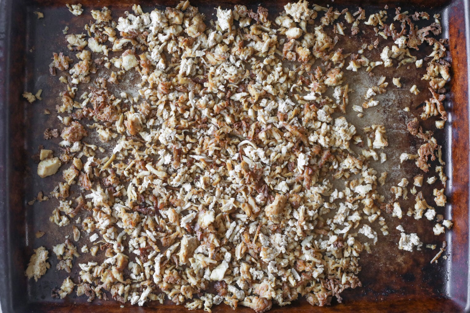 A Baking Sheet Filled With Finely Crumbled, Browned Cauliflower That Appears To Have Been Roasted, Creating A Mix Of Crispy And Tender Pieces—Perfect As A Hearty Topping For A Vegan Chicken Caesar Salad.