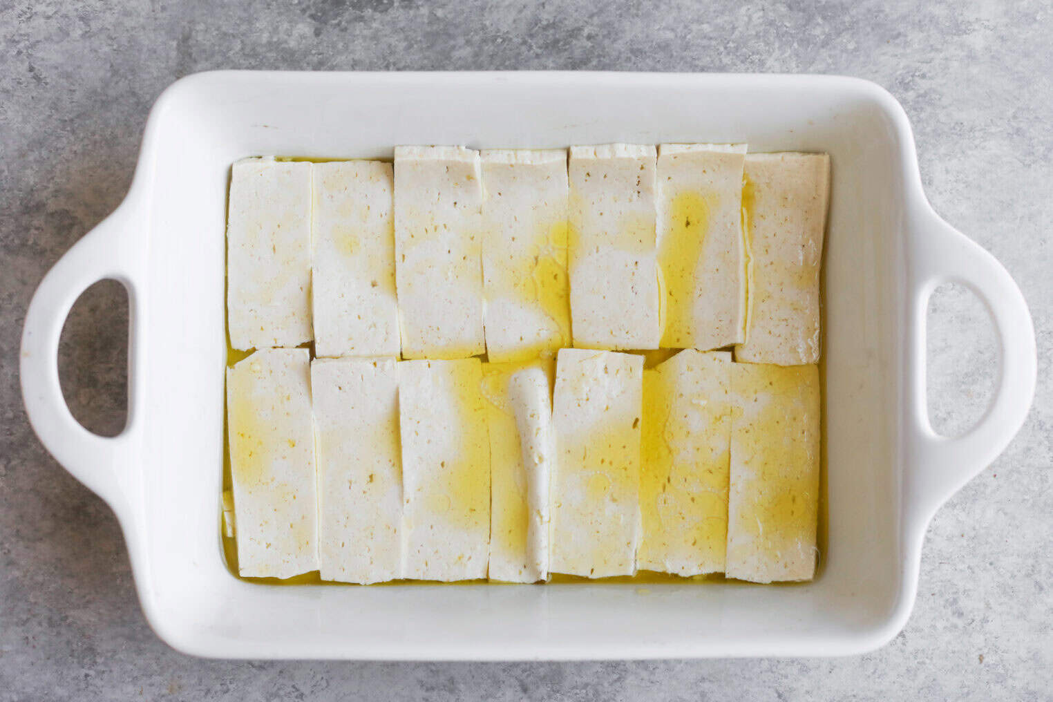 Vegan Italian Panini 4 A White Rectangular Baking Dish Contains Evenly Arranged Slices Of Tofu, Drizzled With Olive Oil, Perfect As A Savory Filling For A Vegan Panini, On A Gray Countertop.