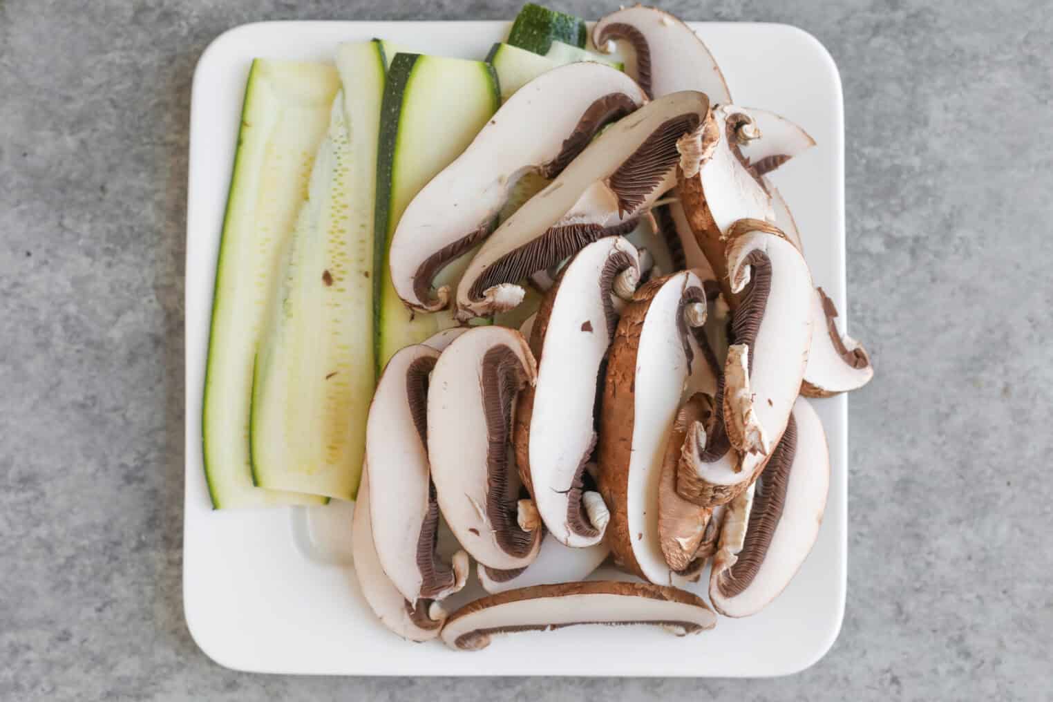 Vegan Italian Panini 5 Sliced Zucchini And Portobello Mushrooms, Perfect For A Vegan Panini, Arranged On A White Square Plate And Placed On A Gray Countertop.