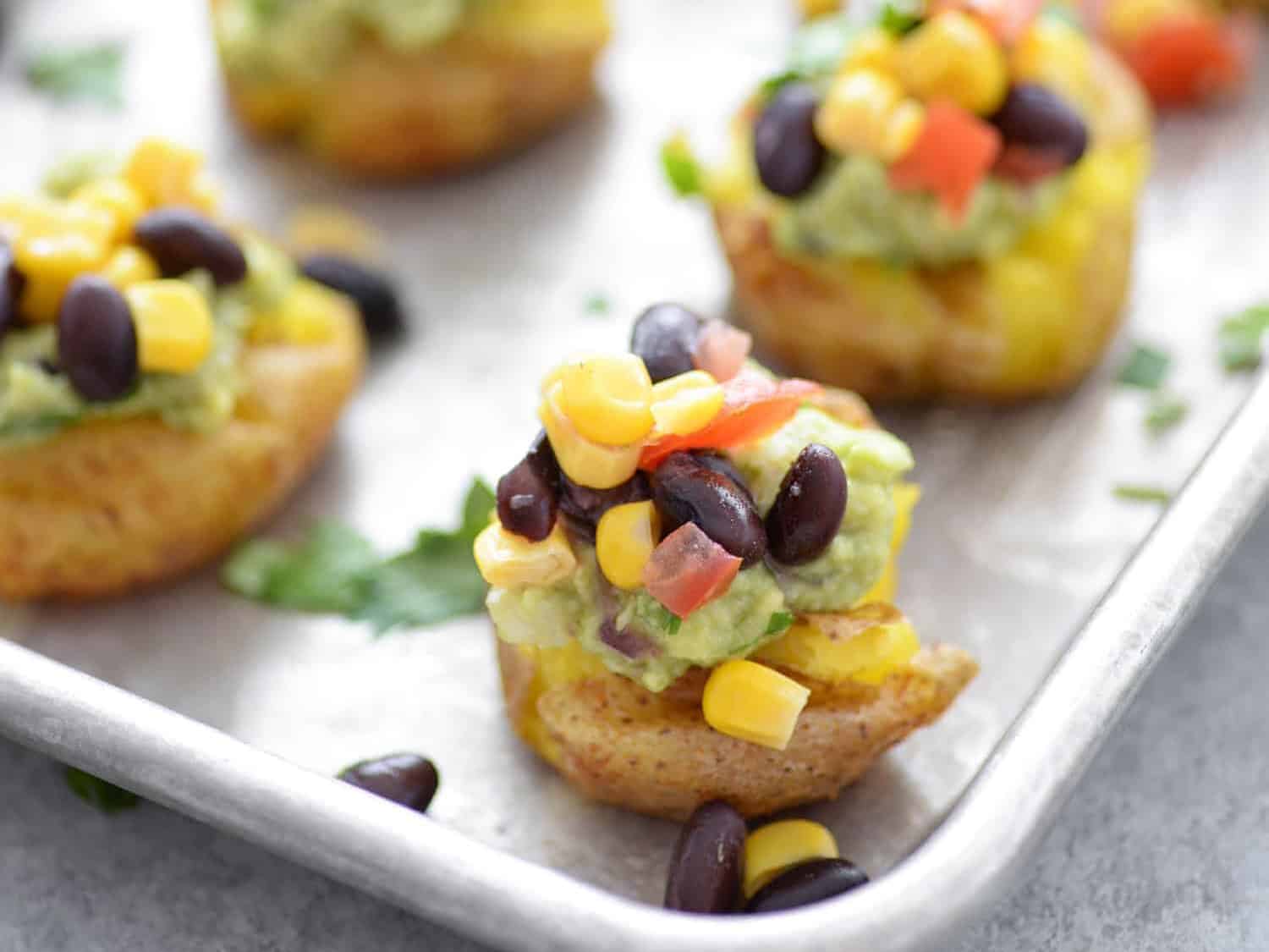 Vegan Loaded Smashed Potatoes! If you are looking for a vegan and gluten-free appetizer, this is it! Smashed potatoes topped with guacamole and corn and bean salsa. A healthy option for football snacks, superbowl and parties. | #superbowl #glutenfree #vegan #vegetarian #appetizer #snack | www.delishknowledge.com