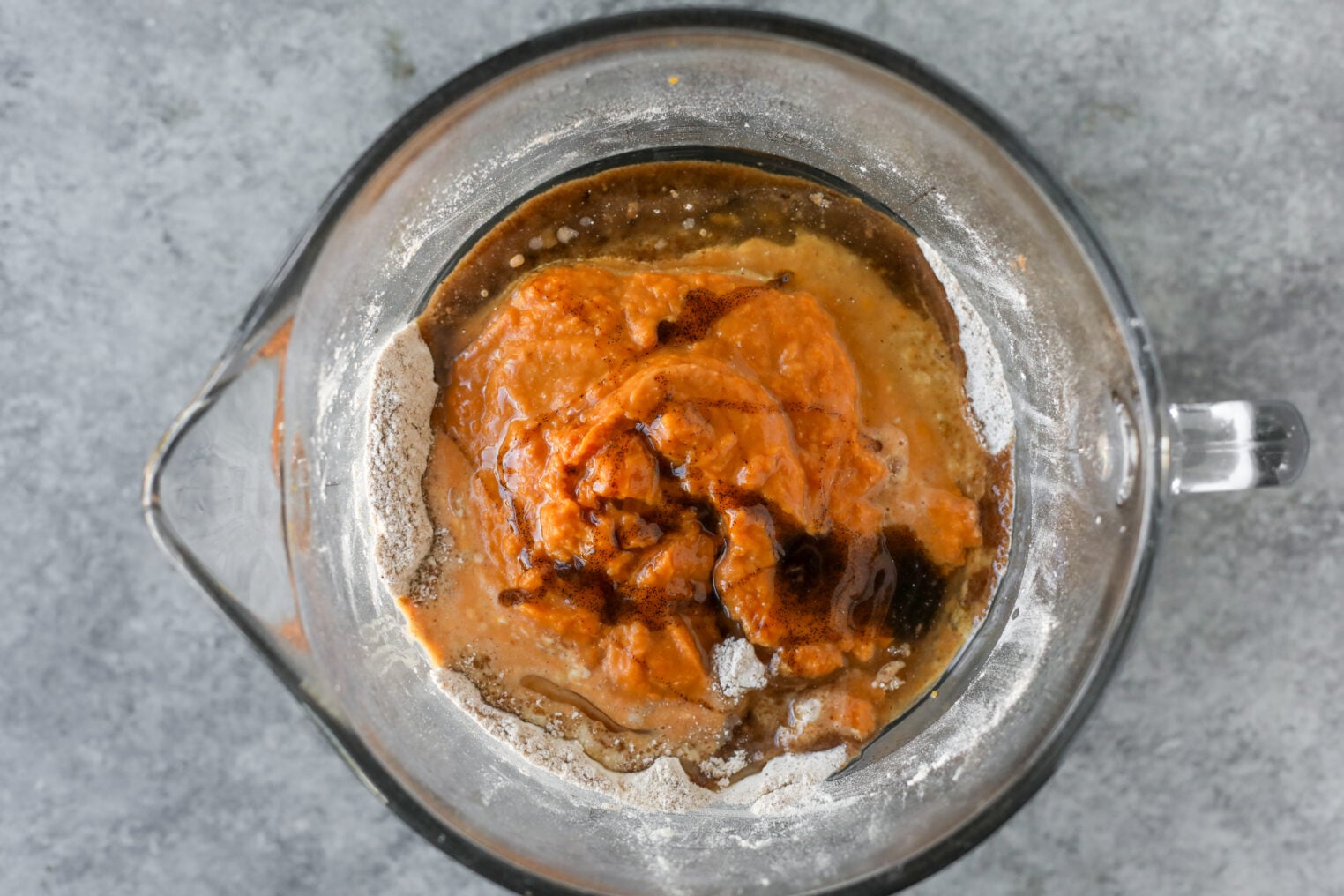 A Glass Mixing Bowl Containing Flour, Pumpkin Puree, And Liquid Ingredients For A Vegan Pumpkin Bread Recipe.