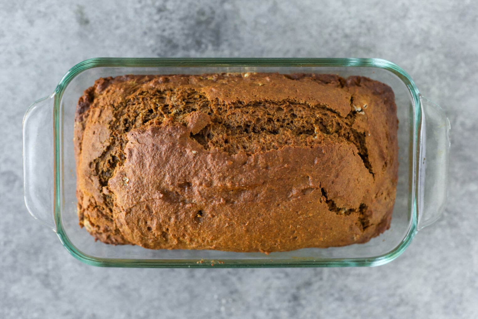 A Loaf Of Vegan Pumpkin Bread Cooling In A Glass Loaf Pan.