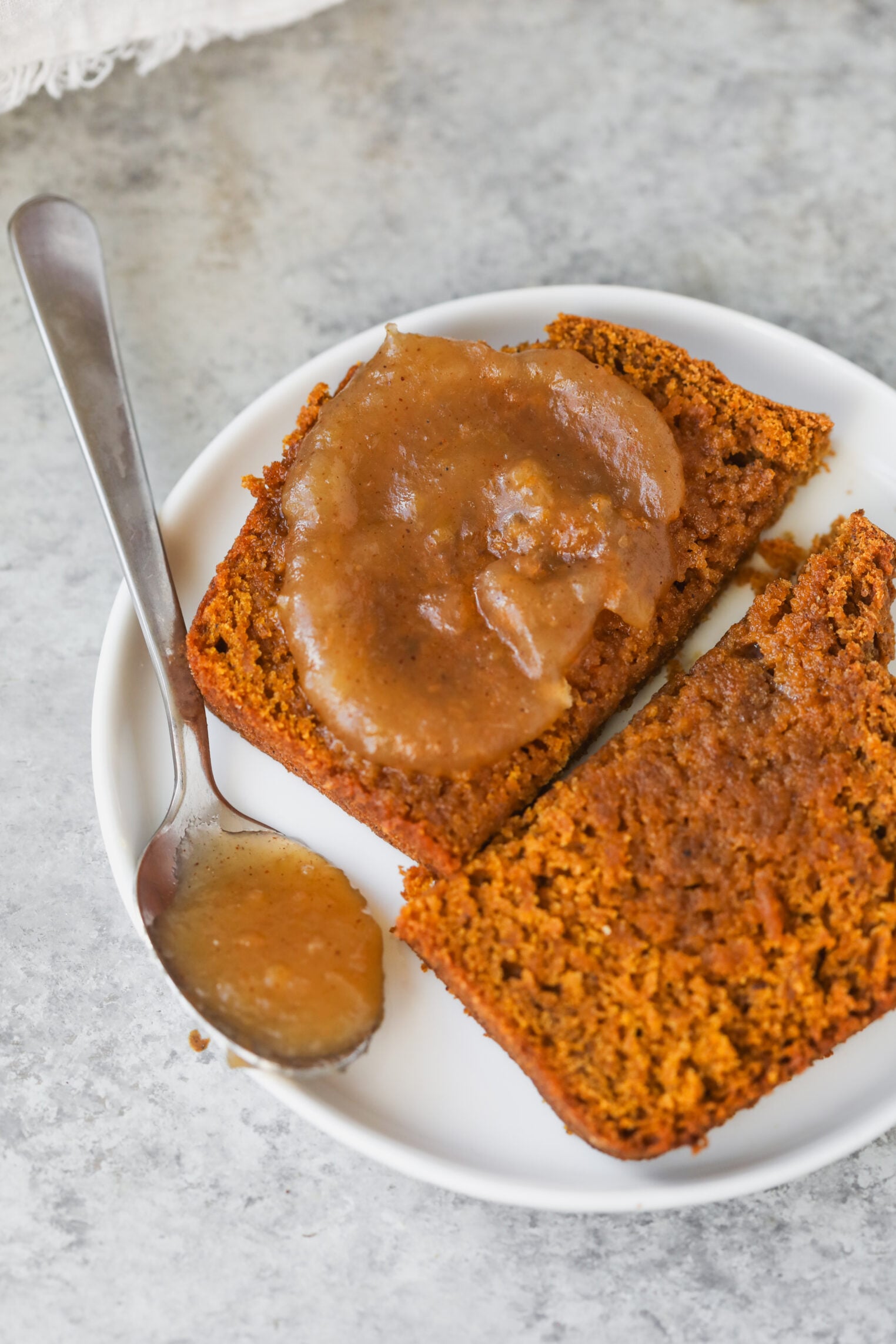 Two Slices Of Vegan Pumpkin Bread On A Small Plate, With Apple Butter Spread On One Slice And A Spoonful Resting On The Side.