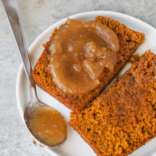 Two Slices Of Vegan Pumpkin Bread On A Small Plate, With Apple Butter Spread On One Slice And A Spoonful Resting On The Side.