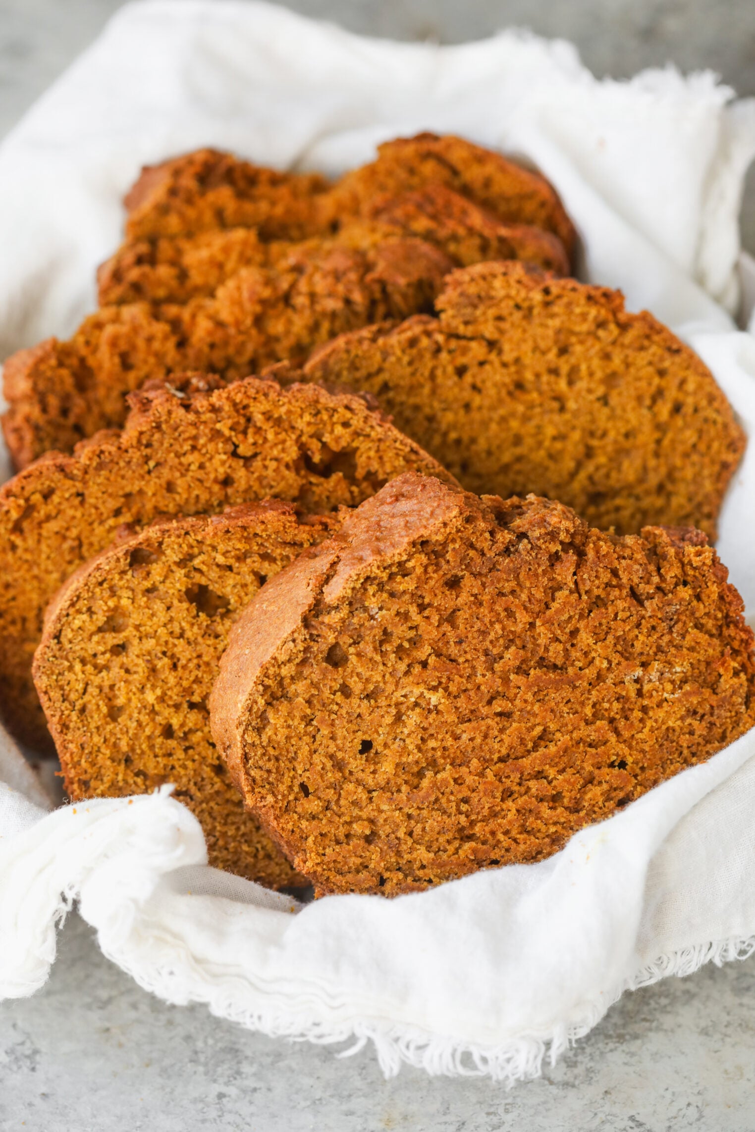 Several Slices Of Dark, Textured Vegan Pumpkin Bread Arranged In A Cloth-Lined Basket.