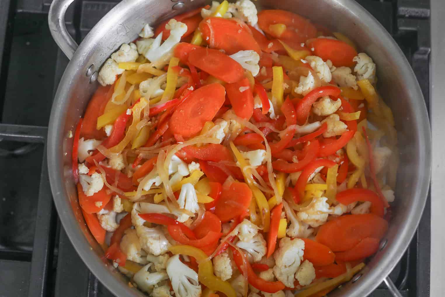 Thai Red Vegetable Curry 6 A Sauté Pan On The Stove Contains A Vibrant Mix Of Sliced Red And Yellow Bell Peppers, Carrots, And Cauliflower Florets, Reminiscent Of A Thai Red Vegetable Curry.